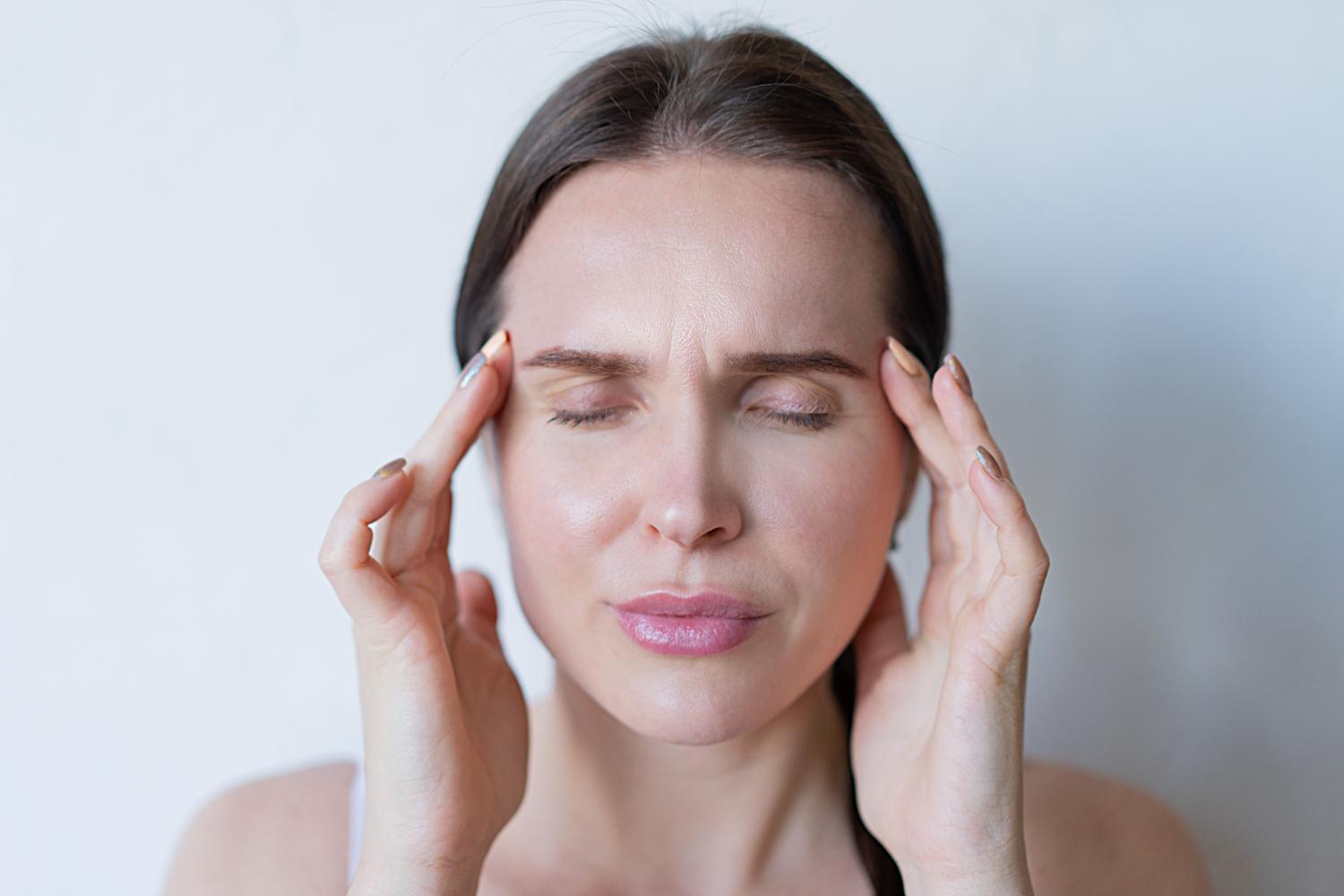 Primer plano de una mujer con los ojos cerrados y las manos en las sienes, sufriendo una migraña intensa.