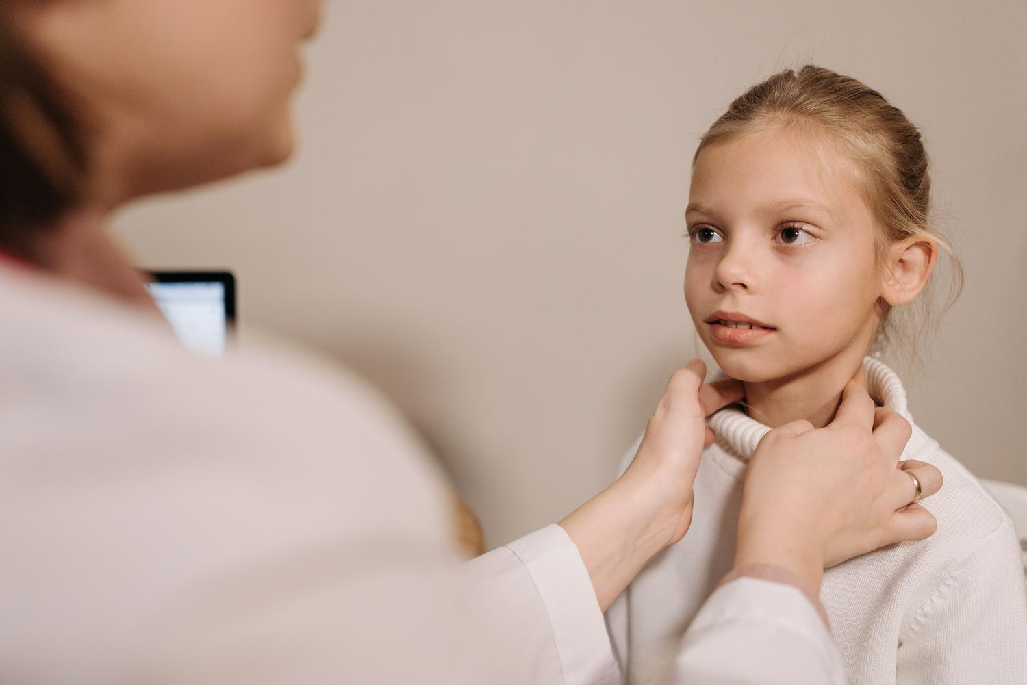 Médico realizando palpación de los ganglios linfáticos cervicales en una niña para detectar adenopatías.