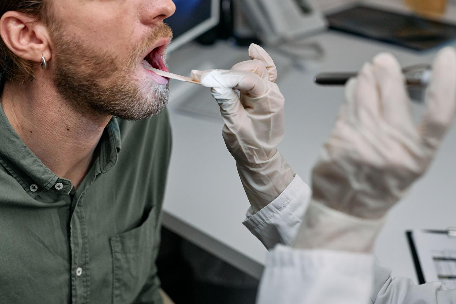 Detalle cercano de un profesional de la salud examinando la cavidad bucal de un paciente con un bajalenguas.