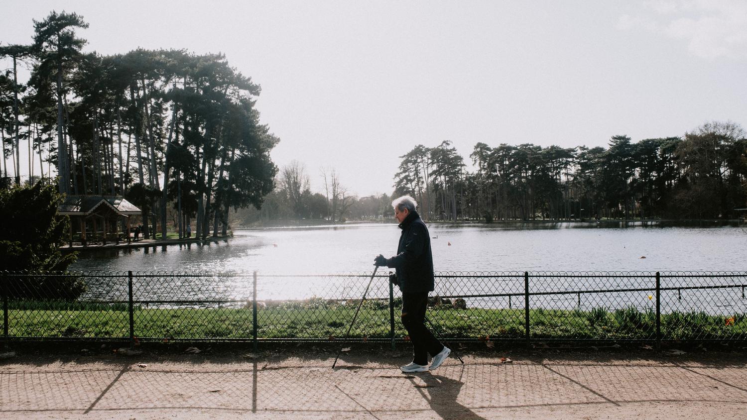 Uma mulher idosa caminhando tranquilamente por um parque, ilustrando a fase de análise da marcha da Escala de Tinetti.