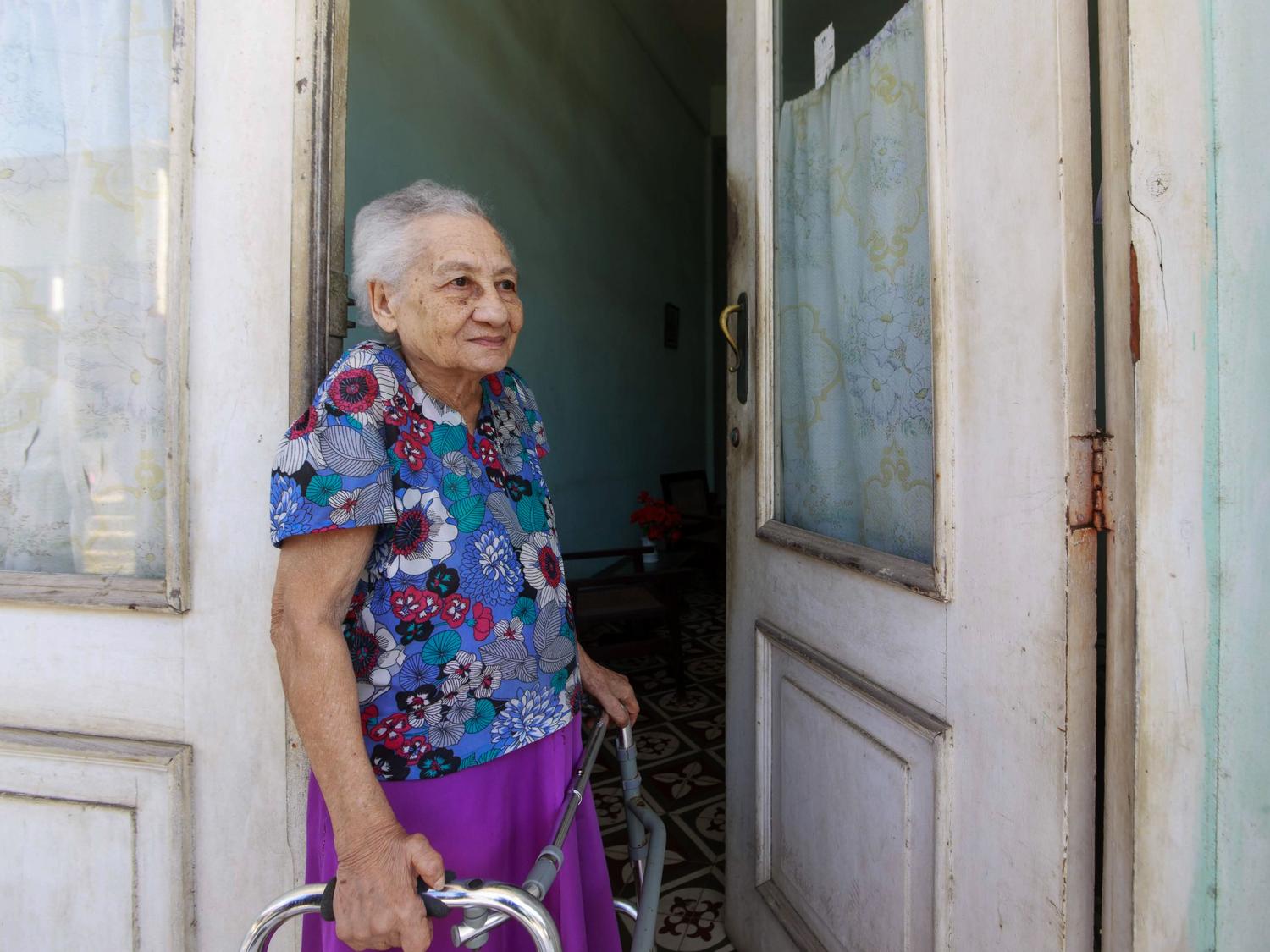 Mujer mayor utilizando un andador en la entrada de su hogar, ilustrando la importancia de la funcionalidad y la adaptación del entorno doméstico.
