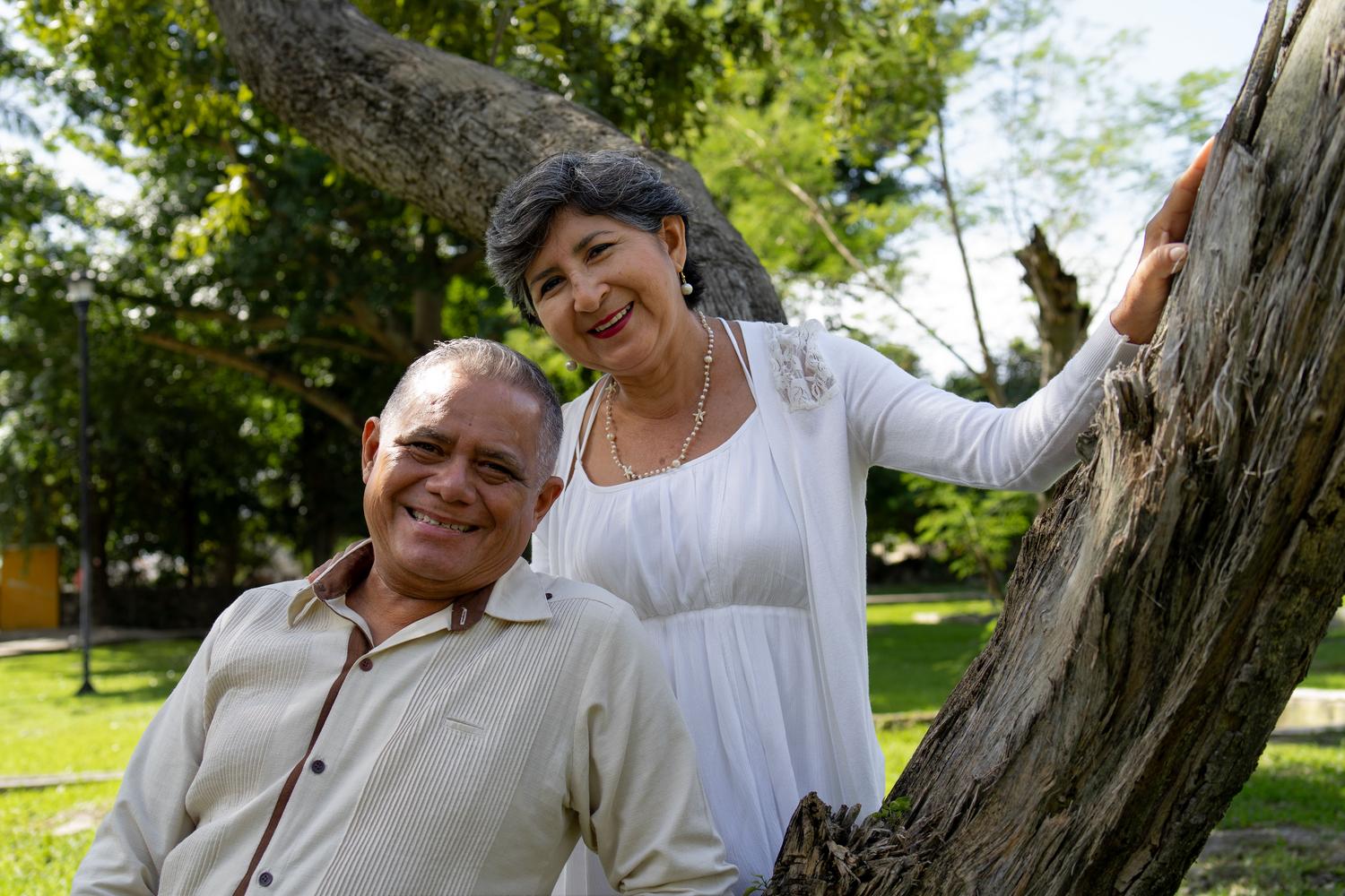 Pareja de adultos mayores sonrientes disfrutando de un día soleado en un parque, representando el envejecimiento saludable y activo.