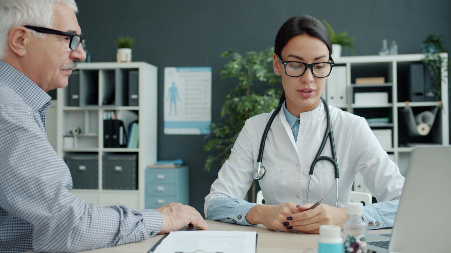 Consulta médica entre uma doutora e um paciente ancião em um consultório moderno, representando a Avaliação Geriátrica Global e a atenção especializada.
