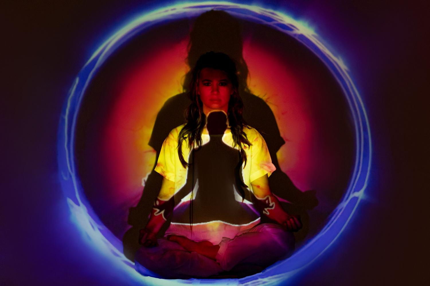 Mujer meditando rodeada de un aura vibrante de energía, simbolizando el proceso de contemplación y el despertar de las claves genéticas espirituales.