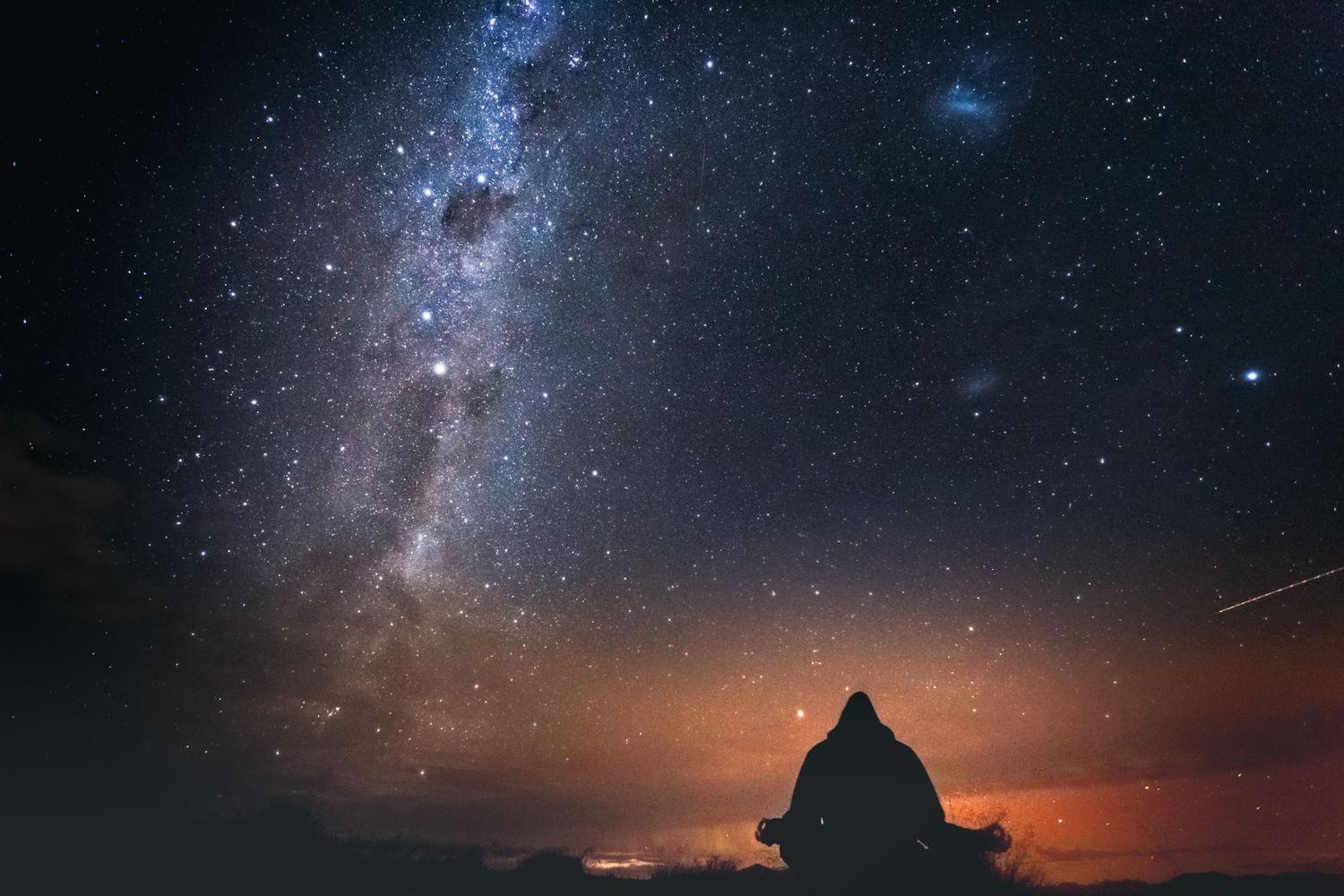 Persona contemplando la Vía Láctea bajo un cielo estrellado, representando la conexión profunda entre nuestro código interno y el universo.