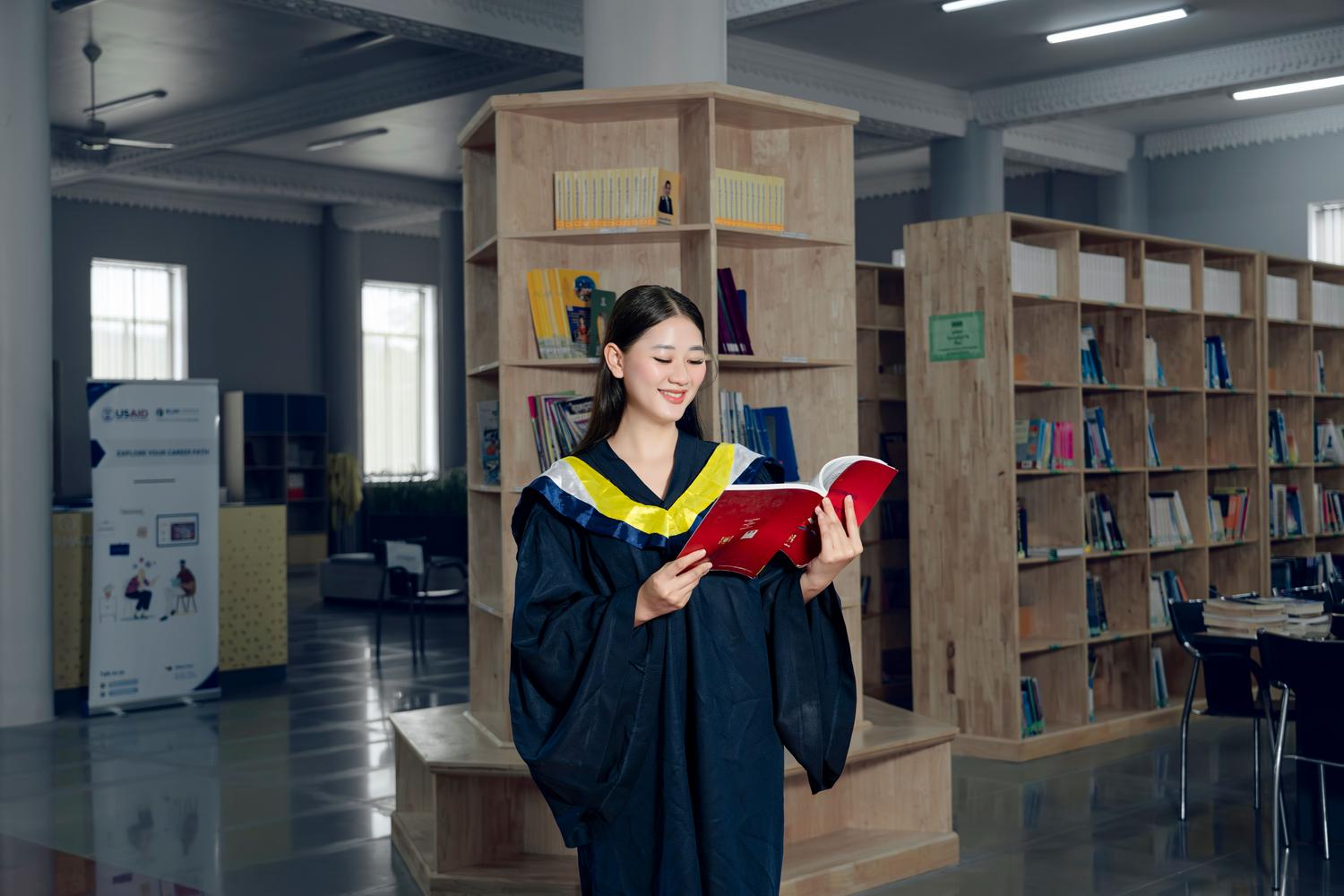 Estudiante con toga académica leyendo un libro en la biblioteca de la universidad, representando el enfoque académico del máster oficial.