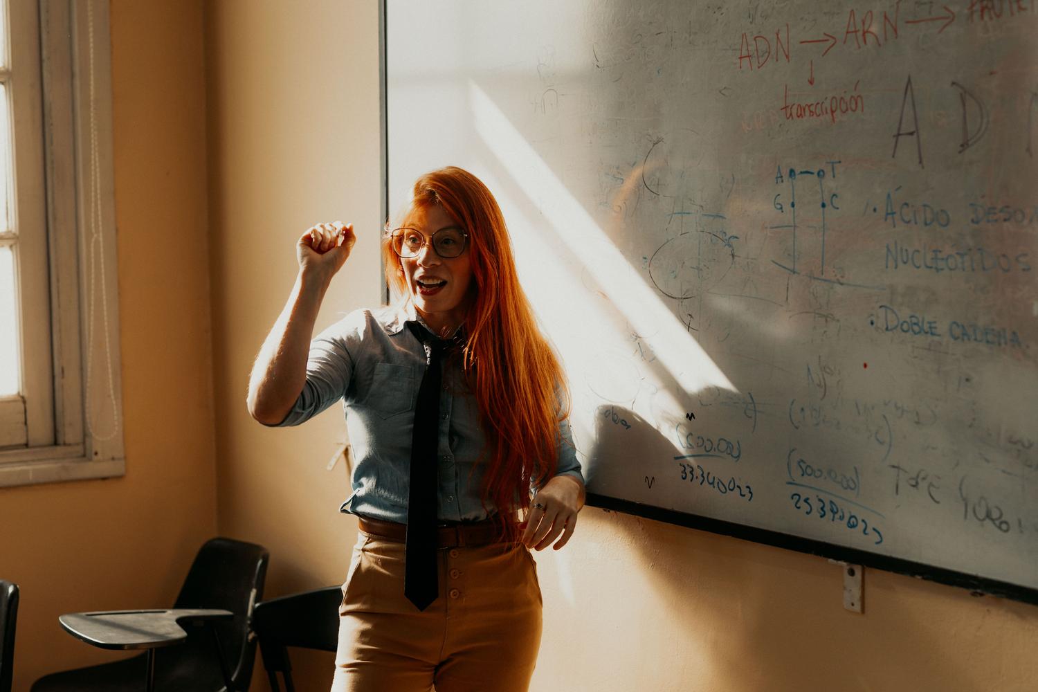 Profesora impartiendo una lección detallada en un aula universitaria, ilustrando la formación teórica y de investigación.