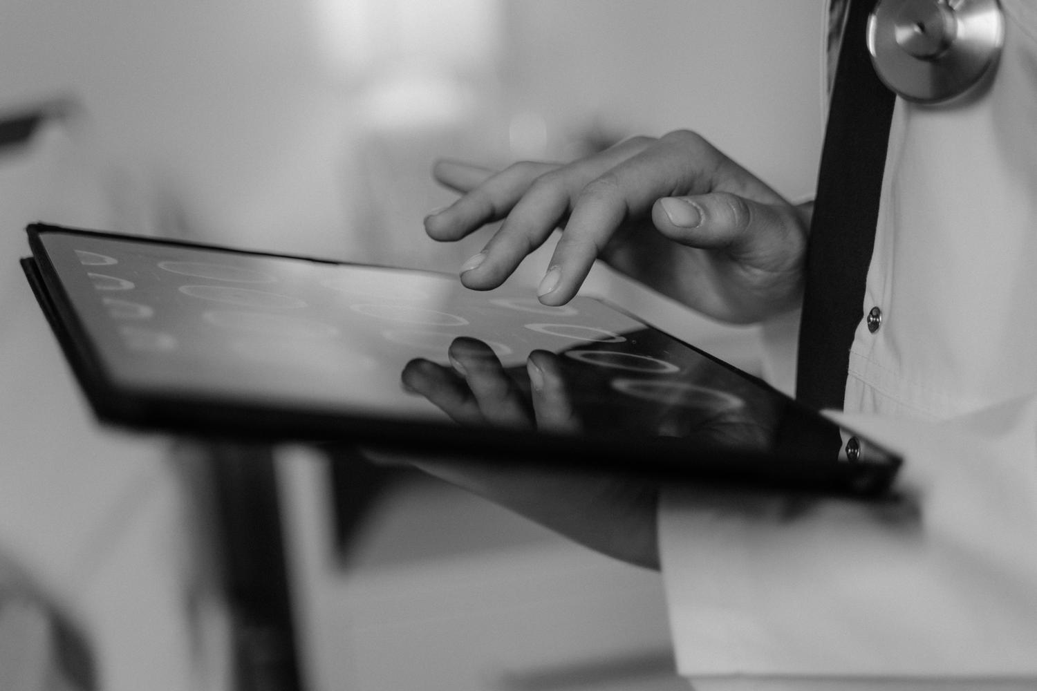 Primer plano en blanco y negro de un médico utilizando uma tablet digital, simbolizando la transición hacia las historias clínicas electrónicas.