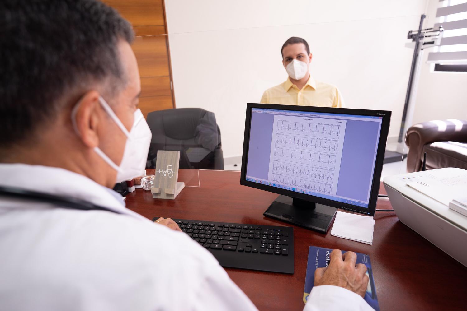 Médico analizando um electrocardiograma digital em um monitor junto a seu paciente, destacando a precisão dos diagnósticos mediante la digitalização.