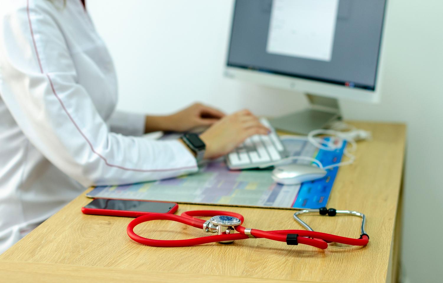 Composição de ferramentas médicas tradicionais e digitais, incluindo um estetoscópio, computador e smartwatch, representando a saúde híbrida e o monitoramento preventivo.