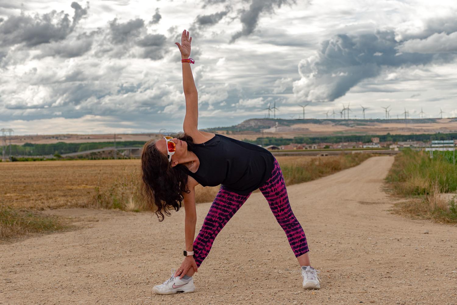 Mujer realizando estiramientos laterales en un camino rural soleado durante el verano