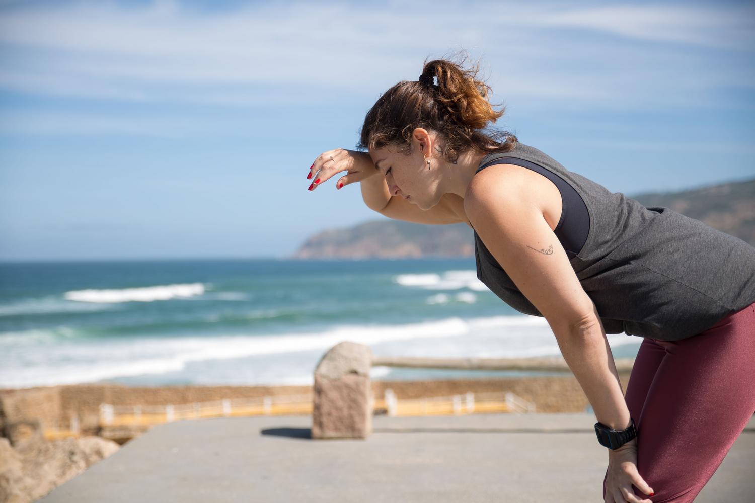 Mujer descansando y recuperando el aliento tras hacer ejercicio frente ao océano en verano