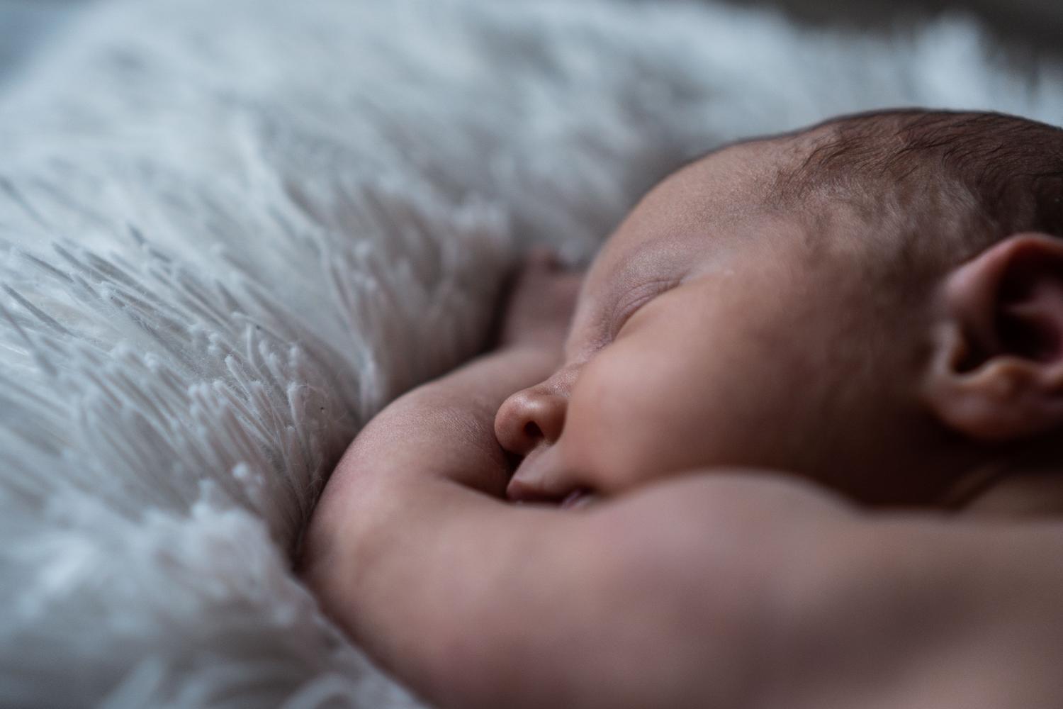 Primer plano de un recién nacido durmiendo plácidamente sobre una manta blanca suave, representando la paz y el descanso neonatal.