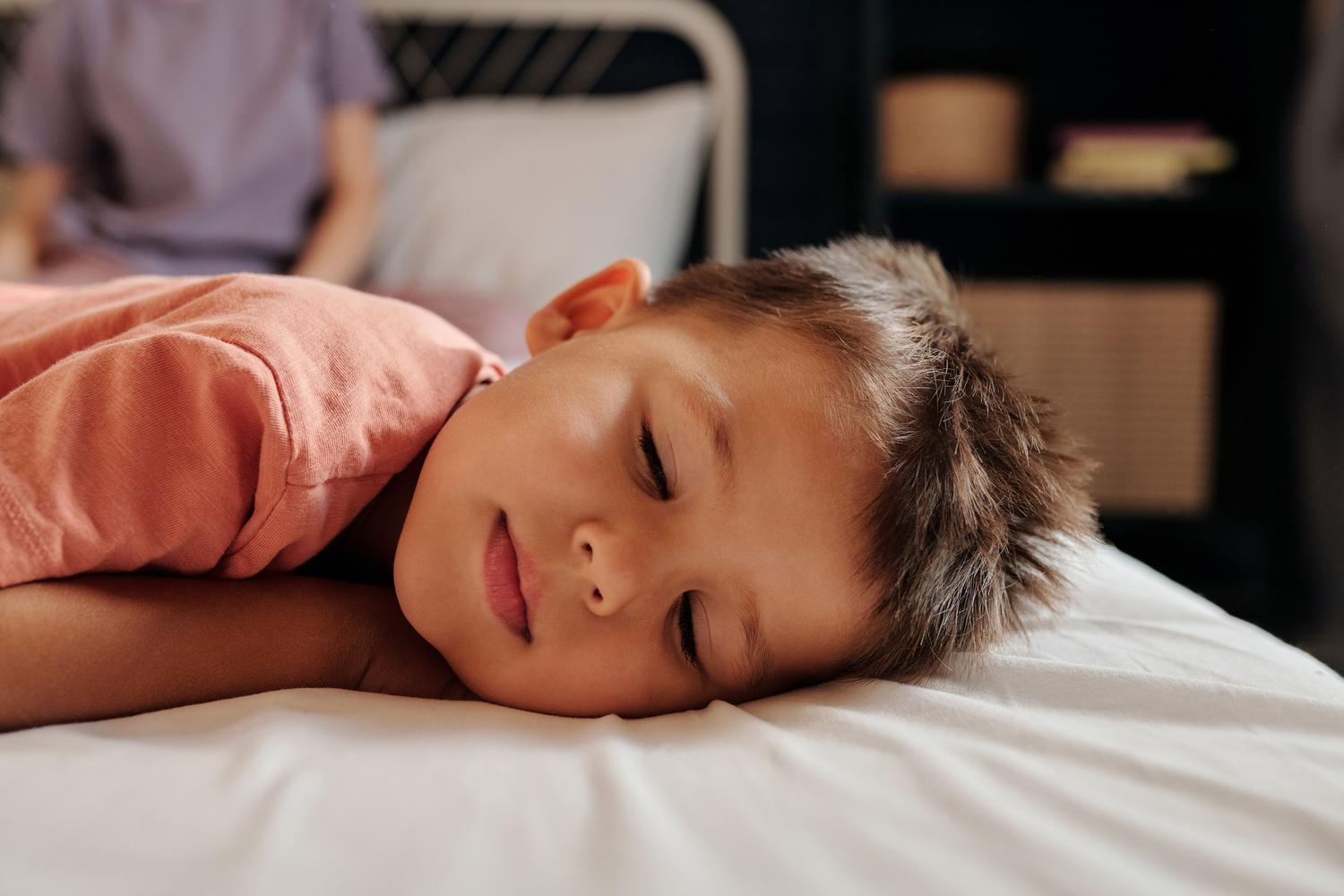 Un niño pequeño durmiendo profundamente em um dormitorio acogedor con iluminación suave, ilustrando el sueño reparador en la infancia.