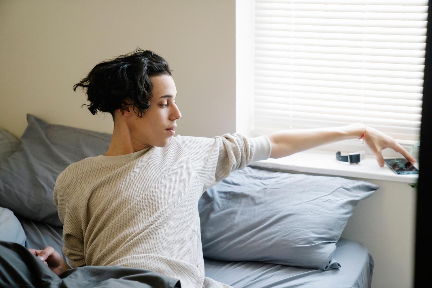 Un adolescente despertando por la mañana y revisando su teléfono móvil, reflejando los ritmos circadianos y el impacto de las pantallas.