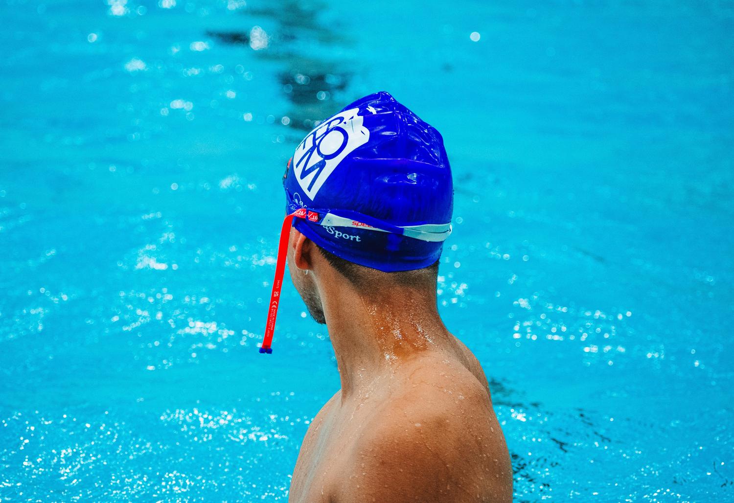 Nadador con gorro de natación azul, ejemplificando la protección recomendada para evitar la entrada de agua.