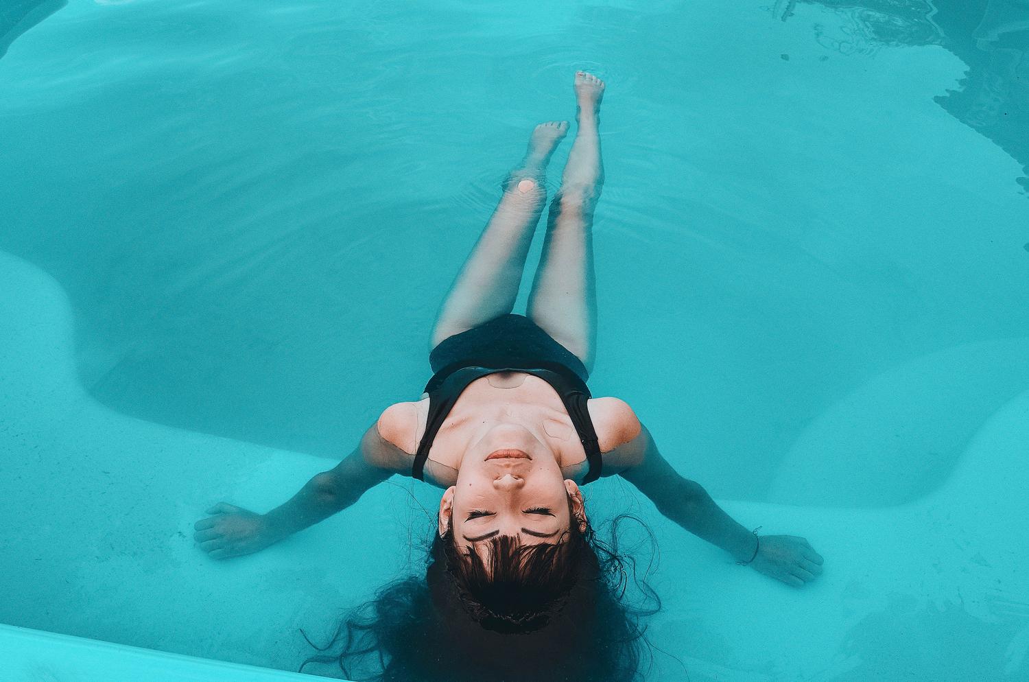 Mujer flotando en una piscina serena, representando el contexto del 'oído del nadador' durante el verano.