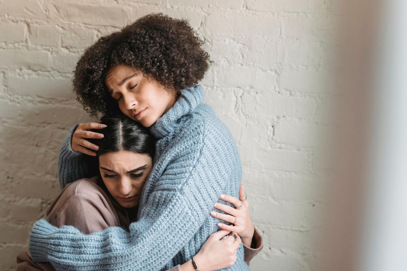 Dos mulheres jovens se abraçando com ternura, representando o apoio emocional e a solidariedade entre amigas em momentos difíceis.