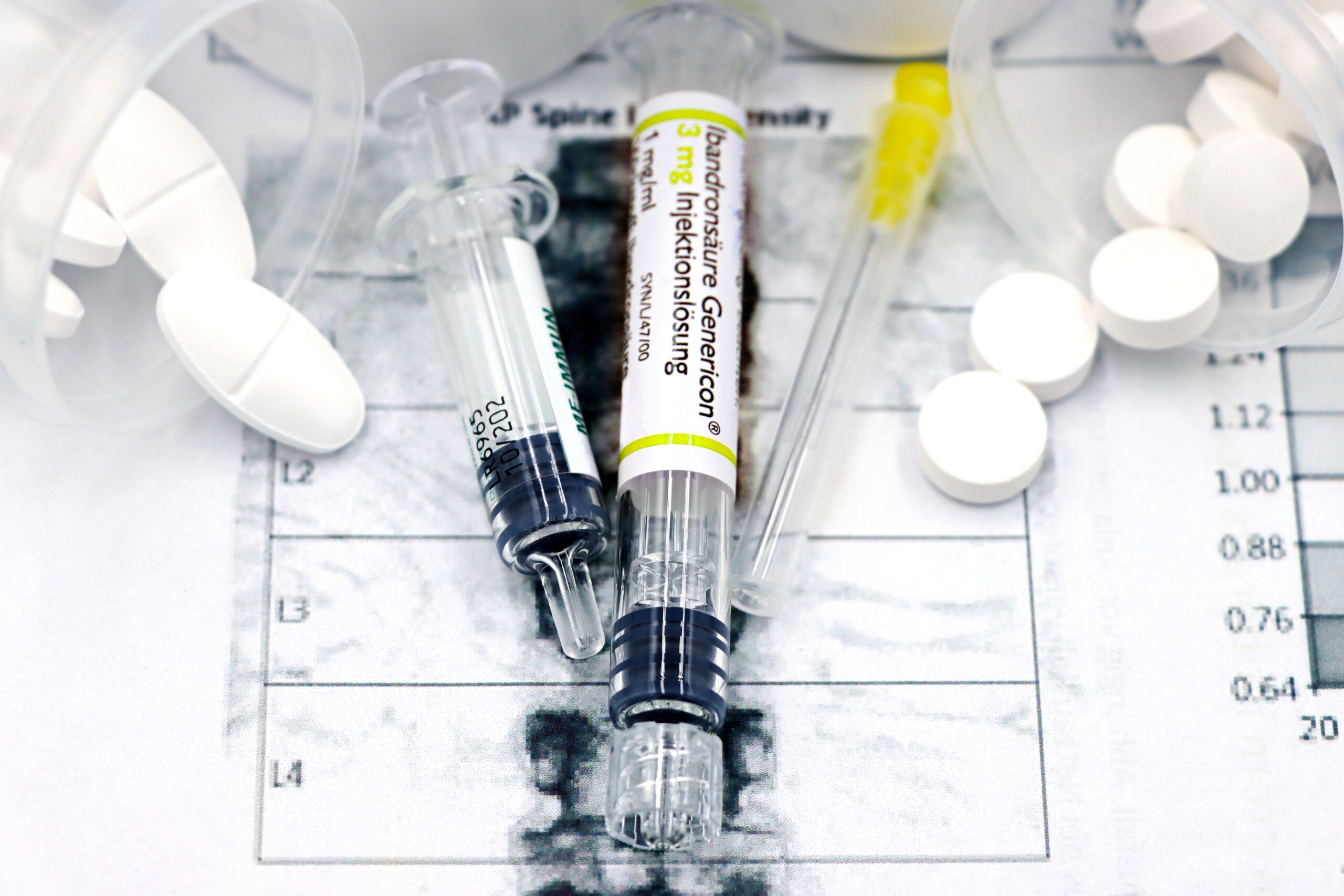 Suministros médicos, incluyendo jeringas de bisfosfonatos y pastillas, sobre un informe de densitometría ósea (DXA).