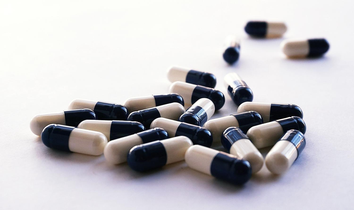 Cápsulas de medicamentos genéricos sobre fundo branco, representando a intervenção farmacológica.
