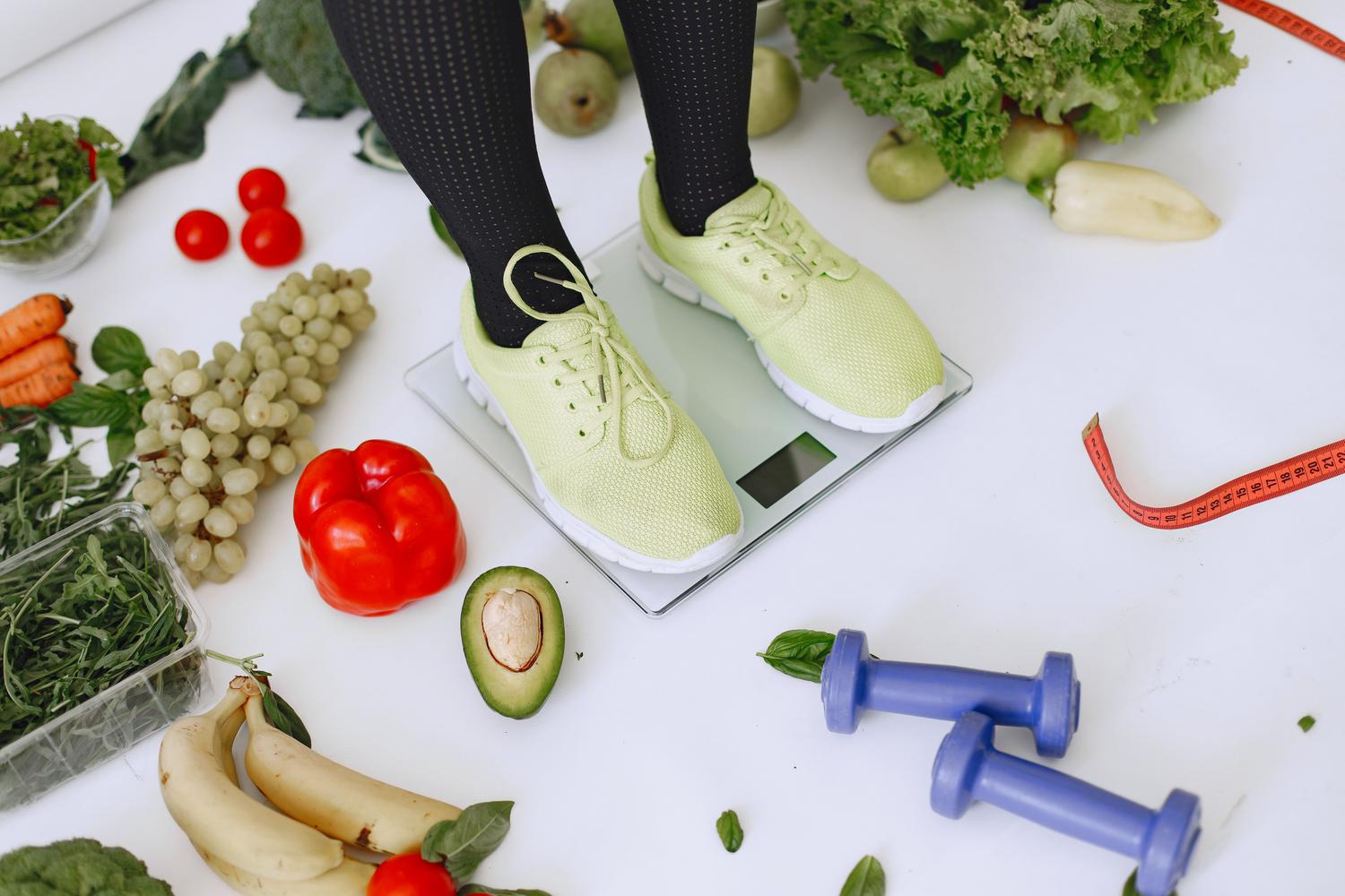 Composição de hábitos saudáveis: balança, alimentos frescos e equipamento de exercício para uma abordagem integral da perda de peso.
