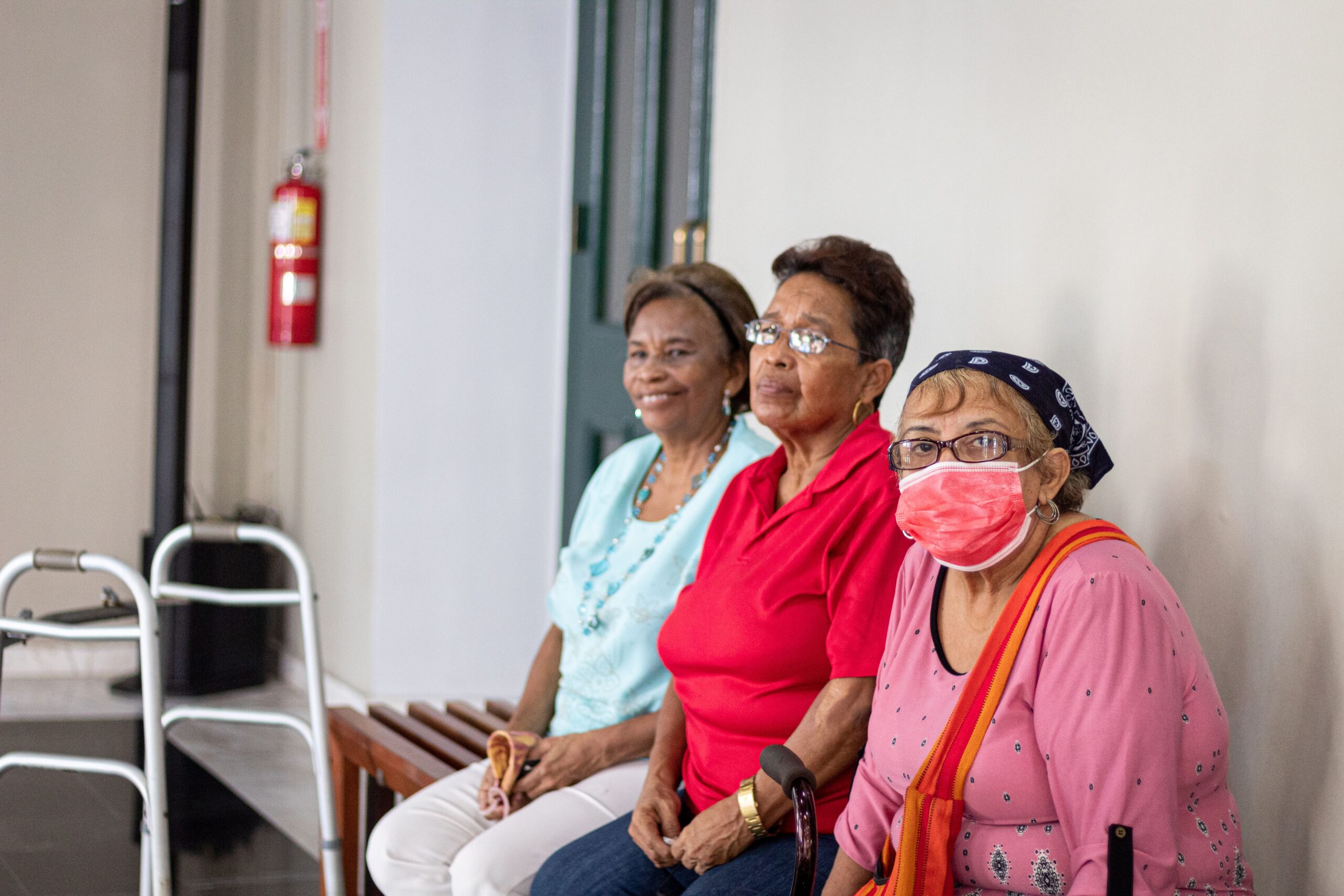 Tres mujeres mayores em um entorno de cuidados, una de ellas utilizando mascarilla quirúrgica.