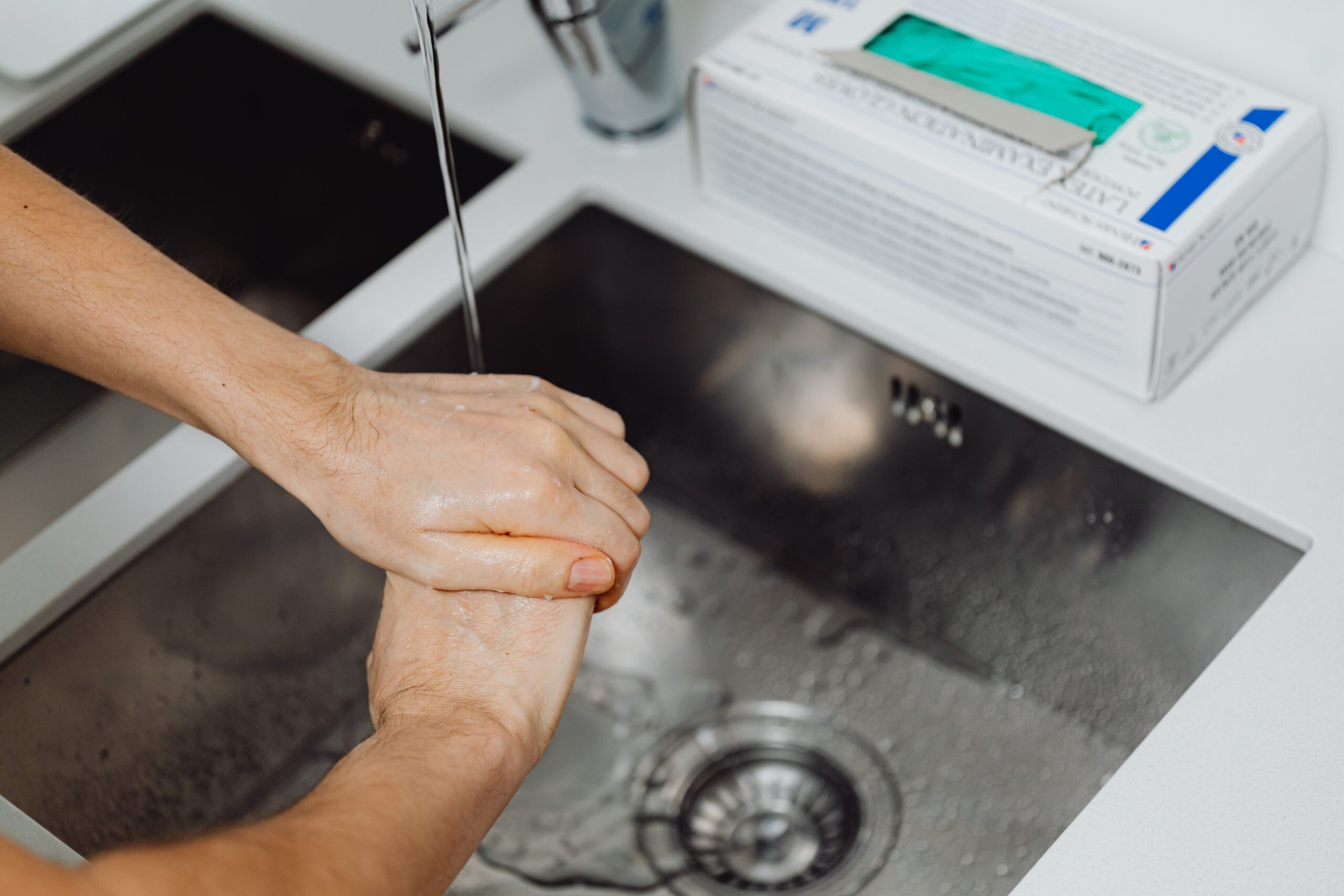 Detalle de manos lavándose con agua y jabón, resaltando la higiene básica como medida de prevención.