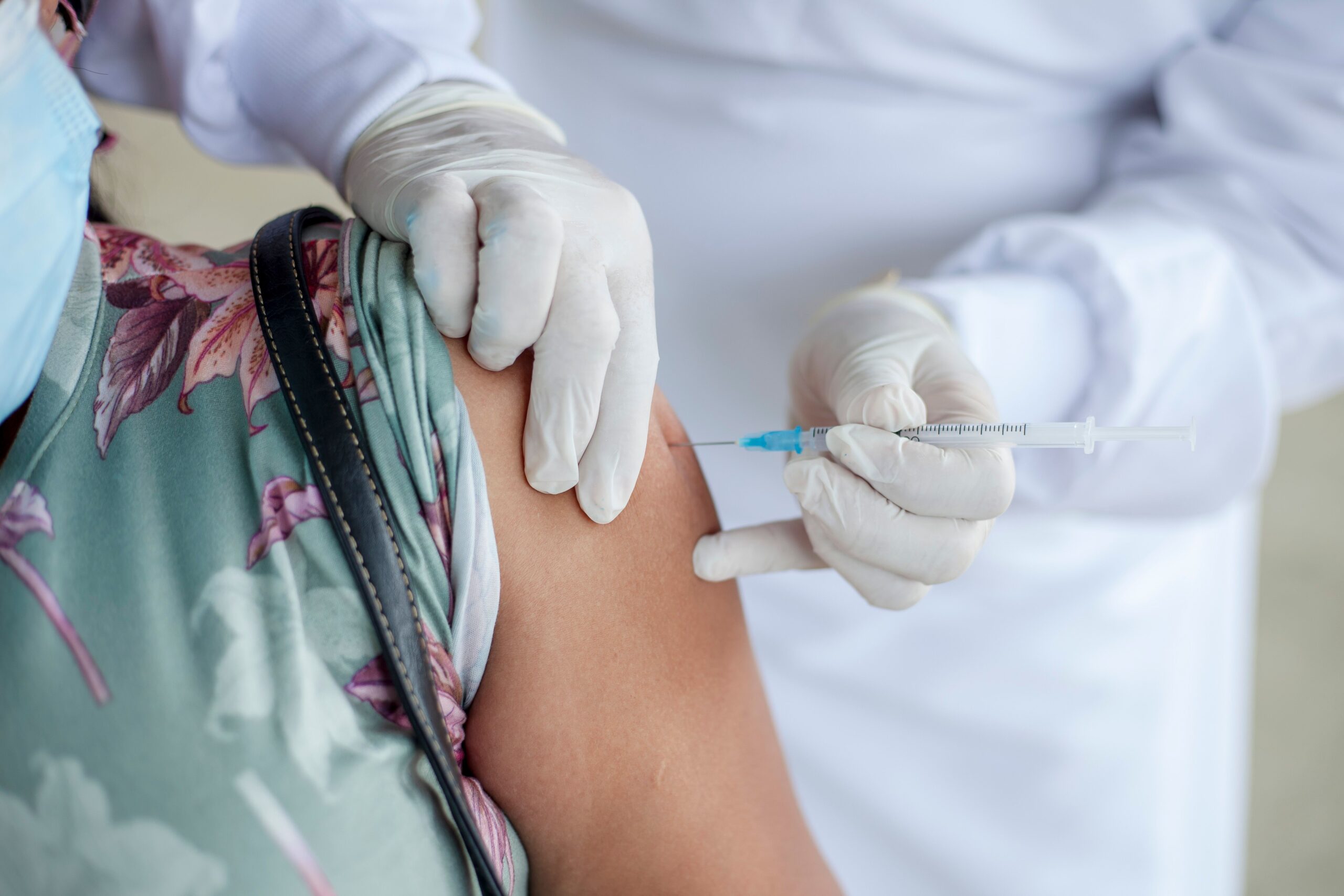 Primer plano de un profesional de la salud administrando una vacuna en el brazo de un paciente que lleva mascarilla.