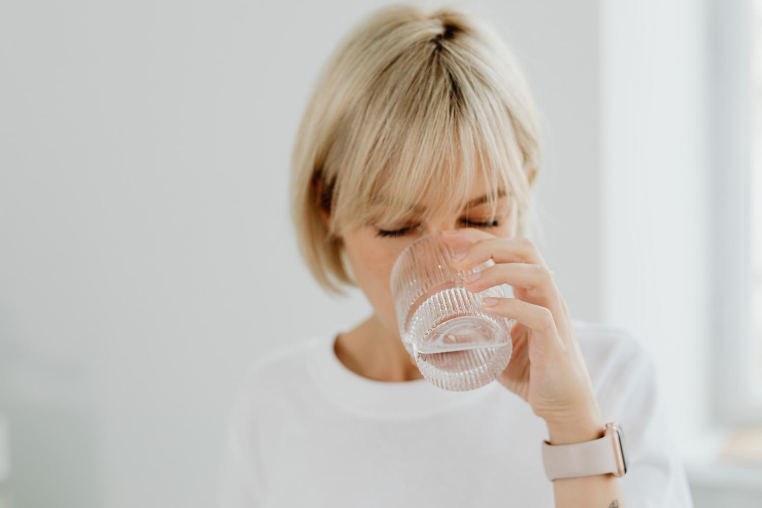 Mujer bebiendo un vaso de água en casa, resaltando la importancia de la hidratación diaria para la salud intestinal.