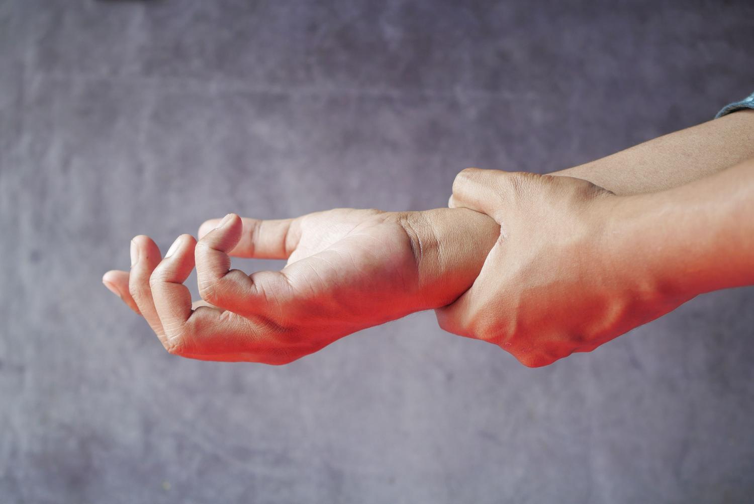 Primer plano de una mano sosteniendo la muñeca con un efecto visual rojo que simboliza la inflamación y el dolor articular, típico de la artritis reumatoide.