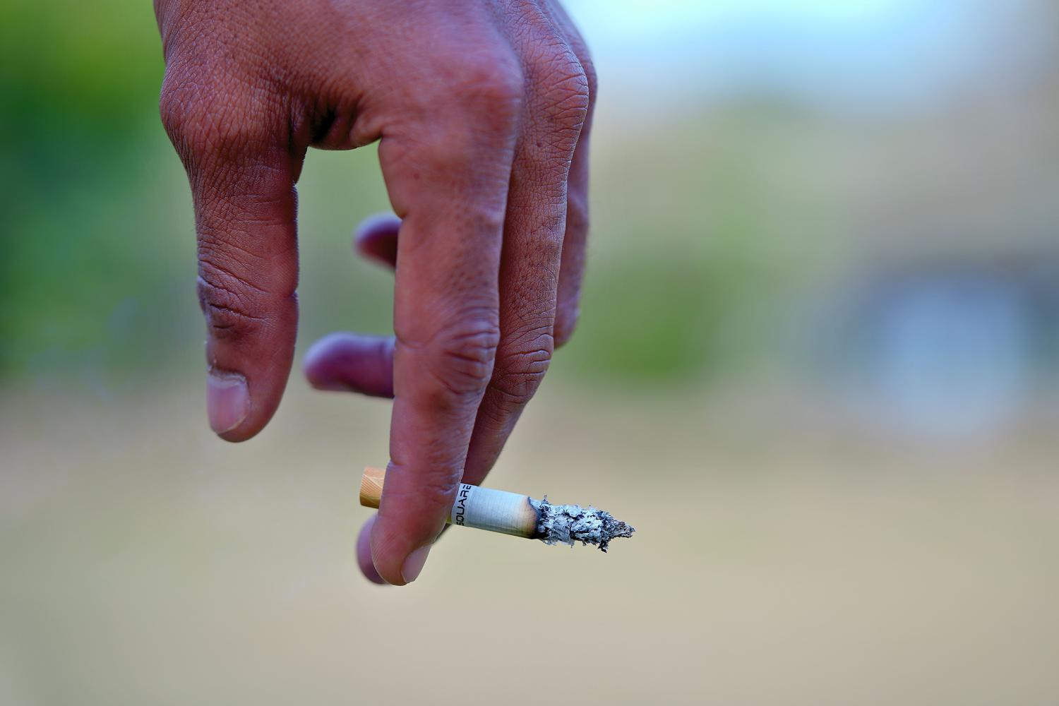 Detalle de una mano sosteniendo un cigarrillo encendido, ilustrando el tabaquismo como uno de los principales factores de riesgo ambientales para desarrollar artritis reumatoide.