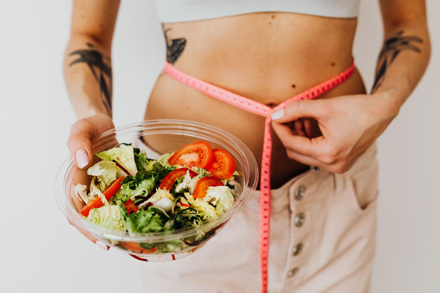 Mujer promoviendo un estilo de vida saludable con una ensalada y medición de cintura, ilustrando la importancia de la pérdida de peso en el tratamiento integral.
