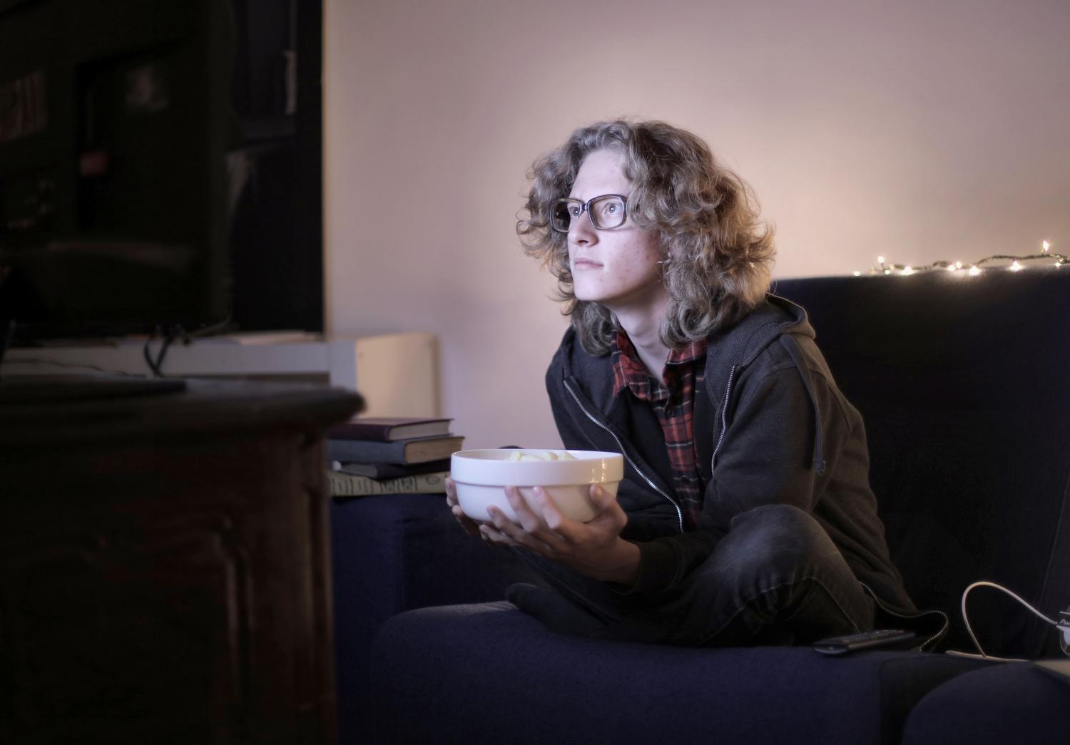 Adolescente concentrado viendo televisión en un salón con luz tenue, reflejando la absorción por los contenidos mediáticos.
