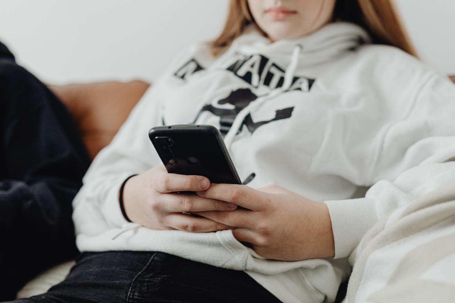 Adolescente con capucha usando su smartphone, transmitiendo una sensación de introspección y soledad moderna en un ambiente doméstico.