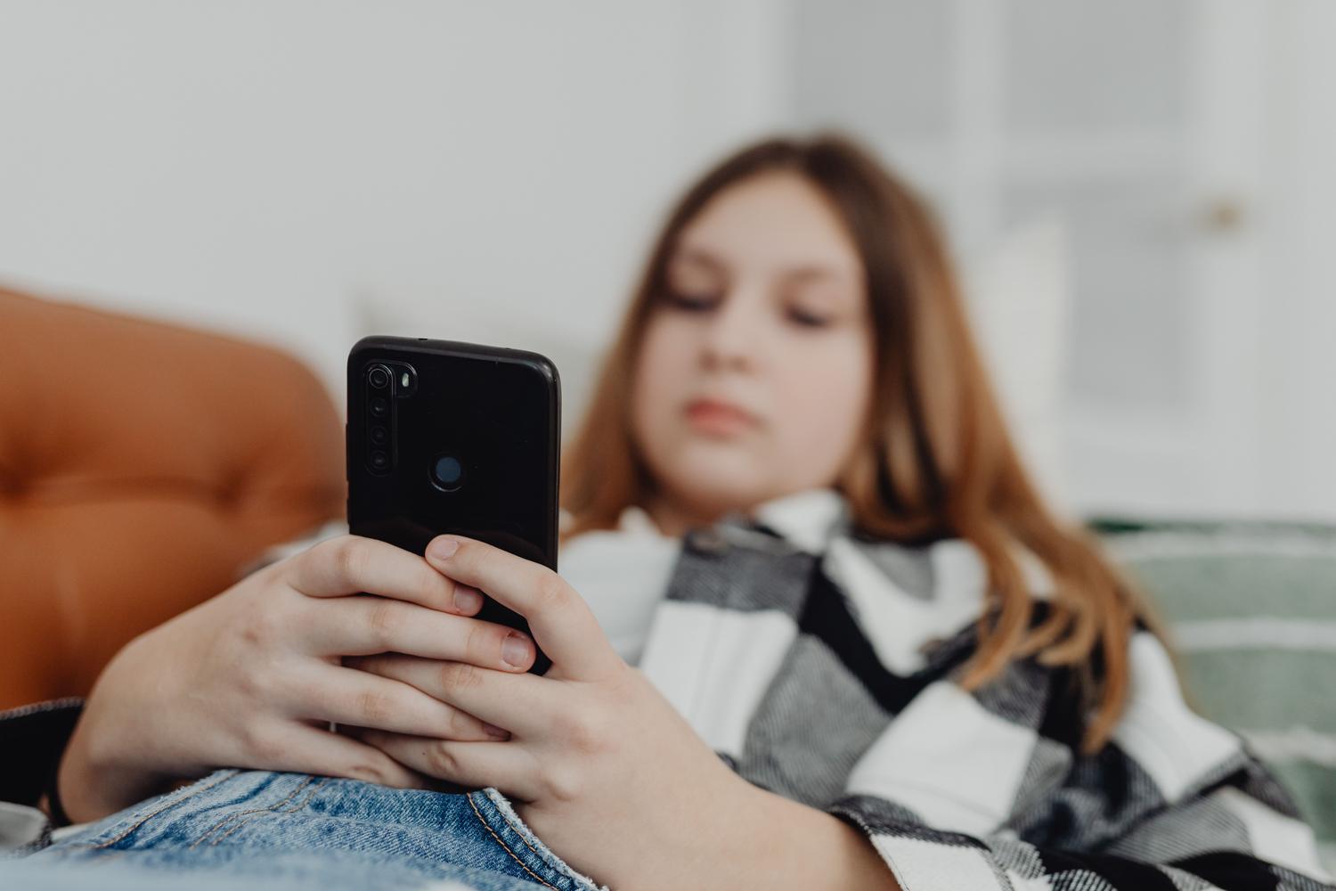 Adolescente absorta en su teléfono móvil sentada en el sofá, representando la desconexión del entorno físico y el aislamiento digital.