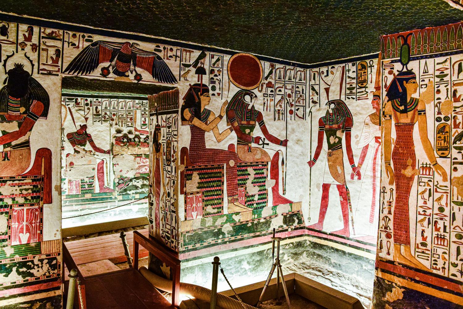 Murales coloridos y vibrantes en el interior de uma tumba egipcia, representando escenas mitológicas y religiosas.