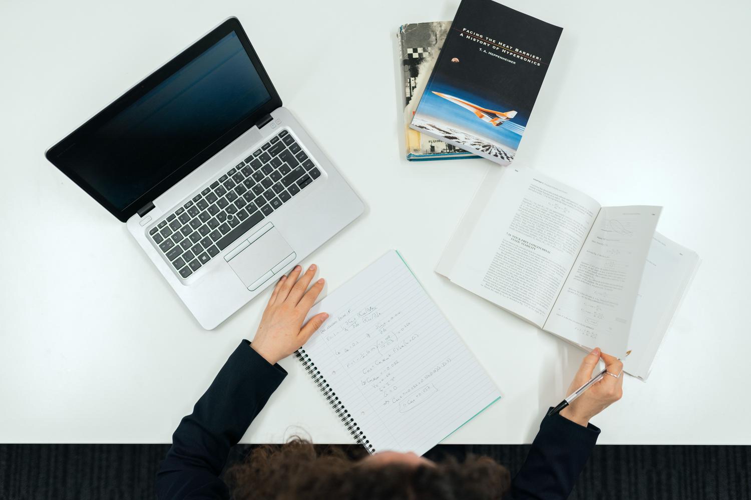 Vista cenital de un escritorio organizado con libros, cuadernos y una laptop, representando la sistematización de la bibliografía.