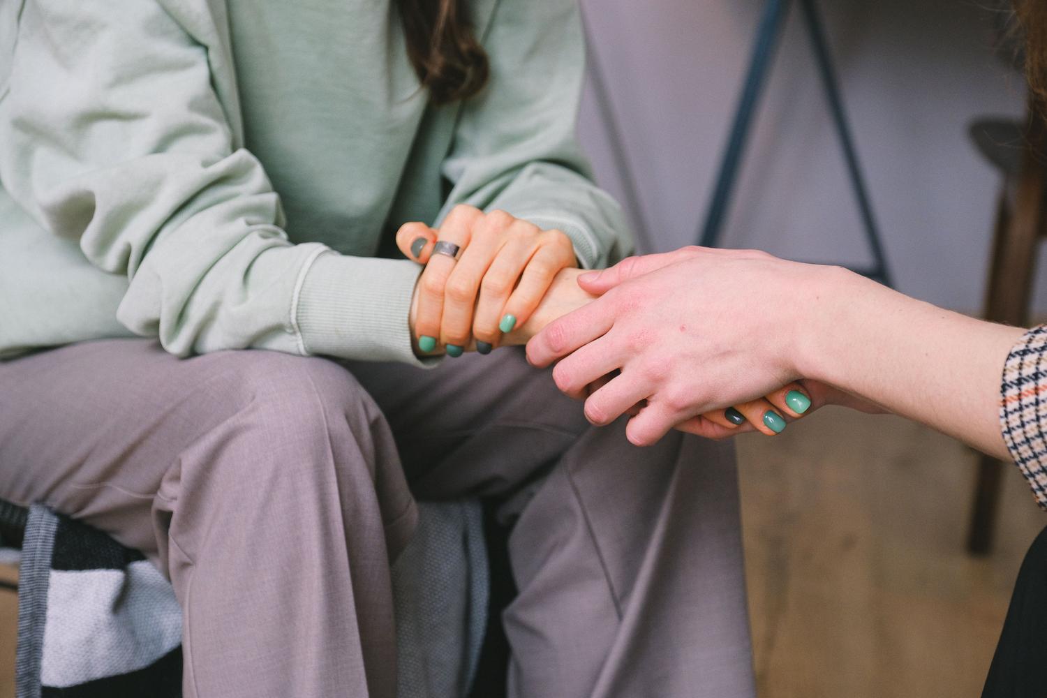 Primer plano de dos personas sosteniendo sus manos en un gesto de consuelo y apoyo emocional.