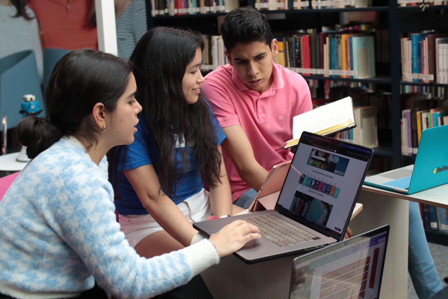 Grupo de estudiantes universitarios colaborando en una biblioteca utilizando laptops y libros físicos para investigar.