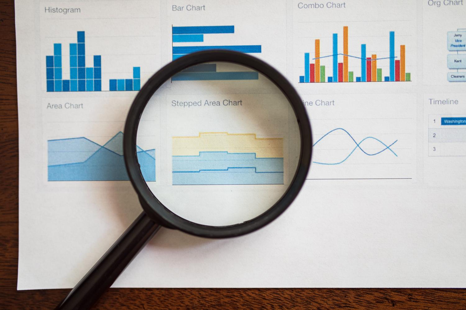 Lupa analizando gráficos de datos, simbolizando el análisis crítico de la información y la lucha contra las noticias falsas.