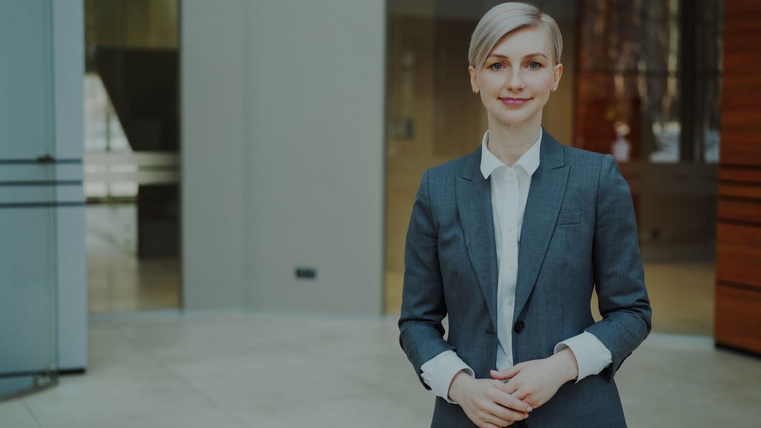 Mujer profesional con traje gris posando con confianza en un entorno corporativo, representando la autonomía y el perfil de Trusted Advisor.