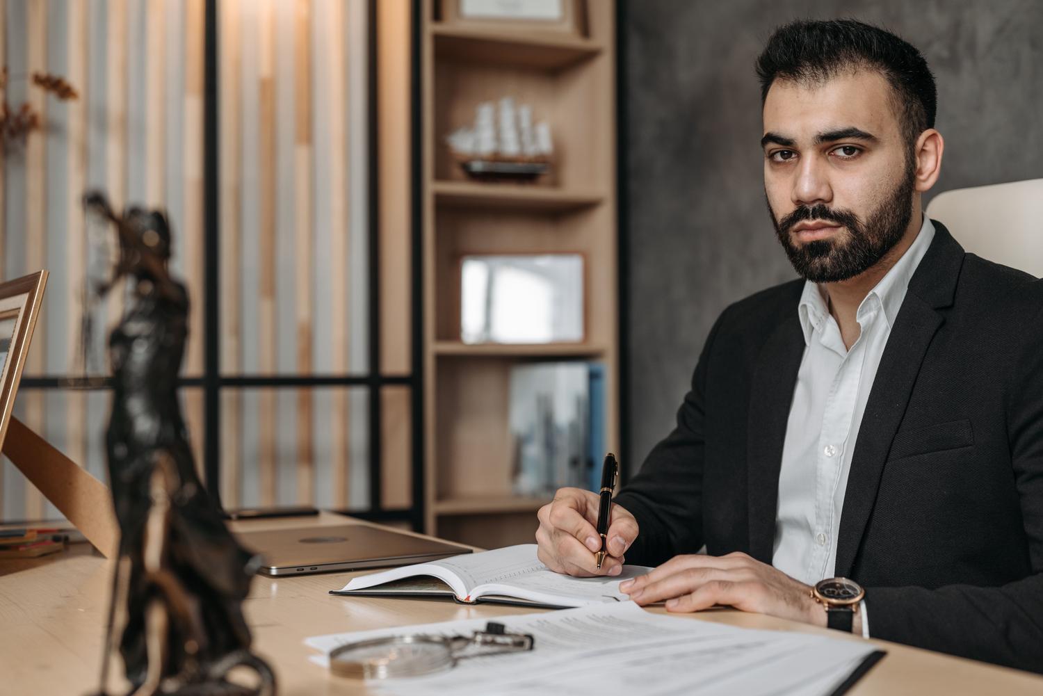 Profesional analizando documentos legales con una lupa y una estatua de la Justicia al fondo en una oficina moderna, representando el análisis regulatorio.