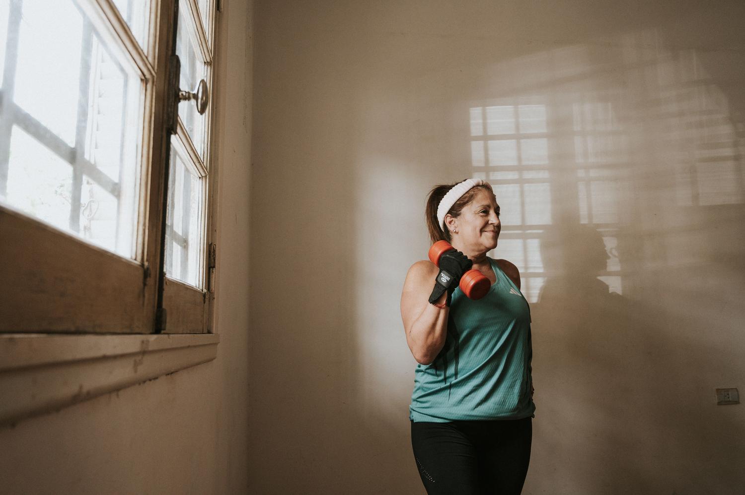 Mujer mayor realizando entrenamiento de fuerza con mancuernas, ejemplificando la prevención y el envejecimiento activo para evitar la cronificación.