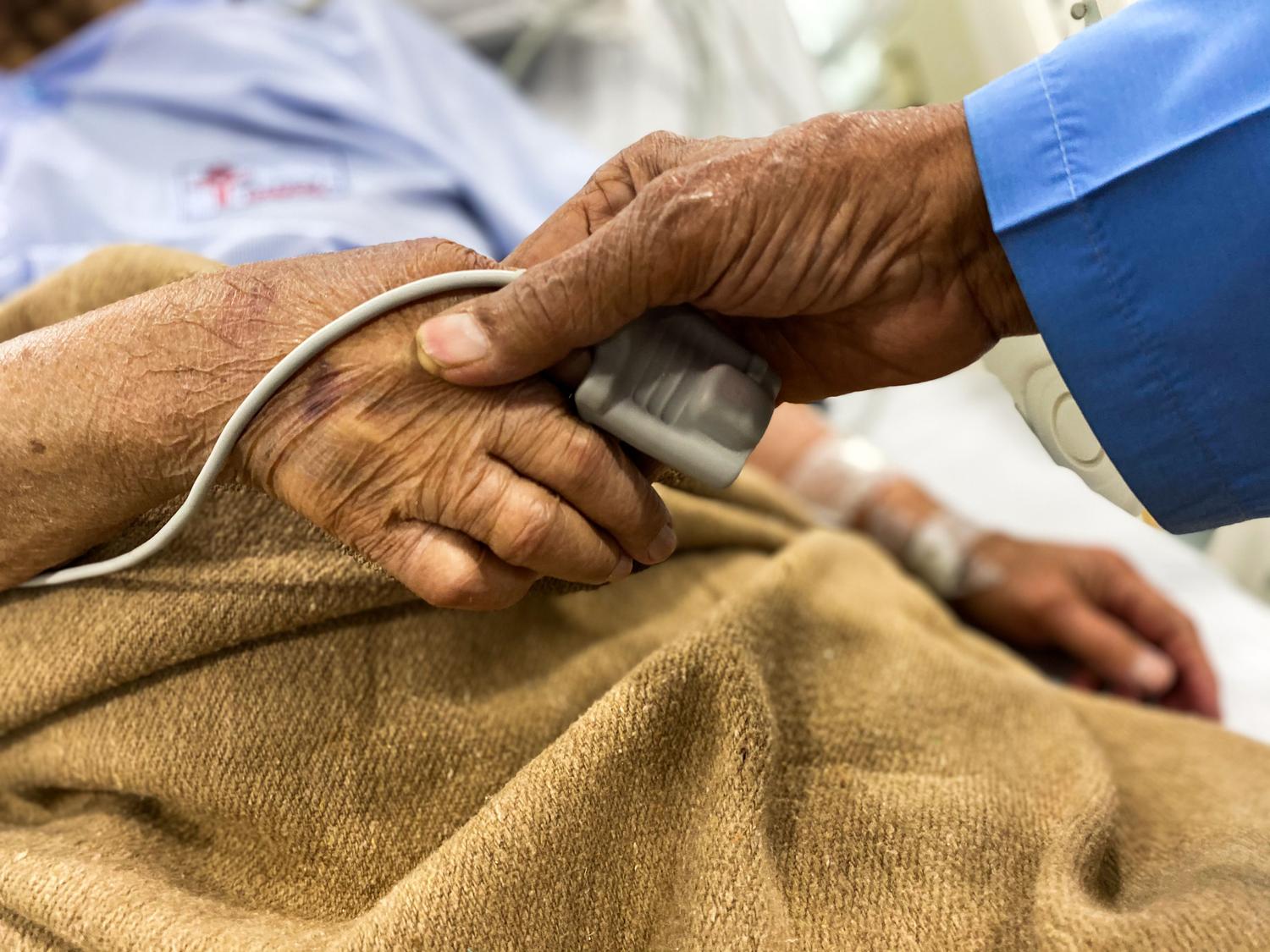 Primer plano de una mano sosteniendo la de un paciente anciano en un entorno hospitalario, simbolizando la dignidad y el cuidado paliativo.
