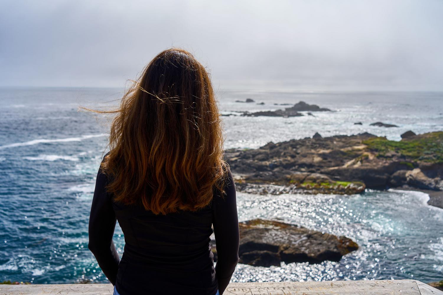 Mujer contemplando o océano desde un acantilado, simbolizando la soledad consciente y la desconexión digital.