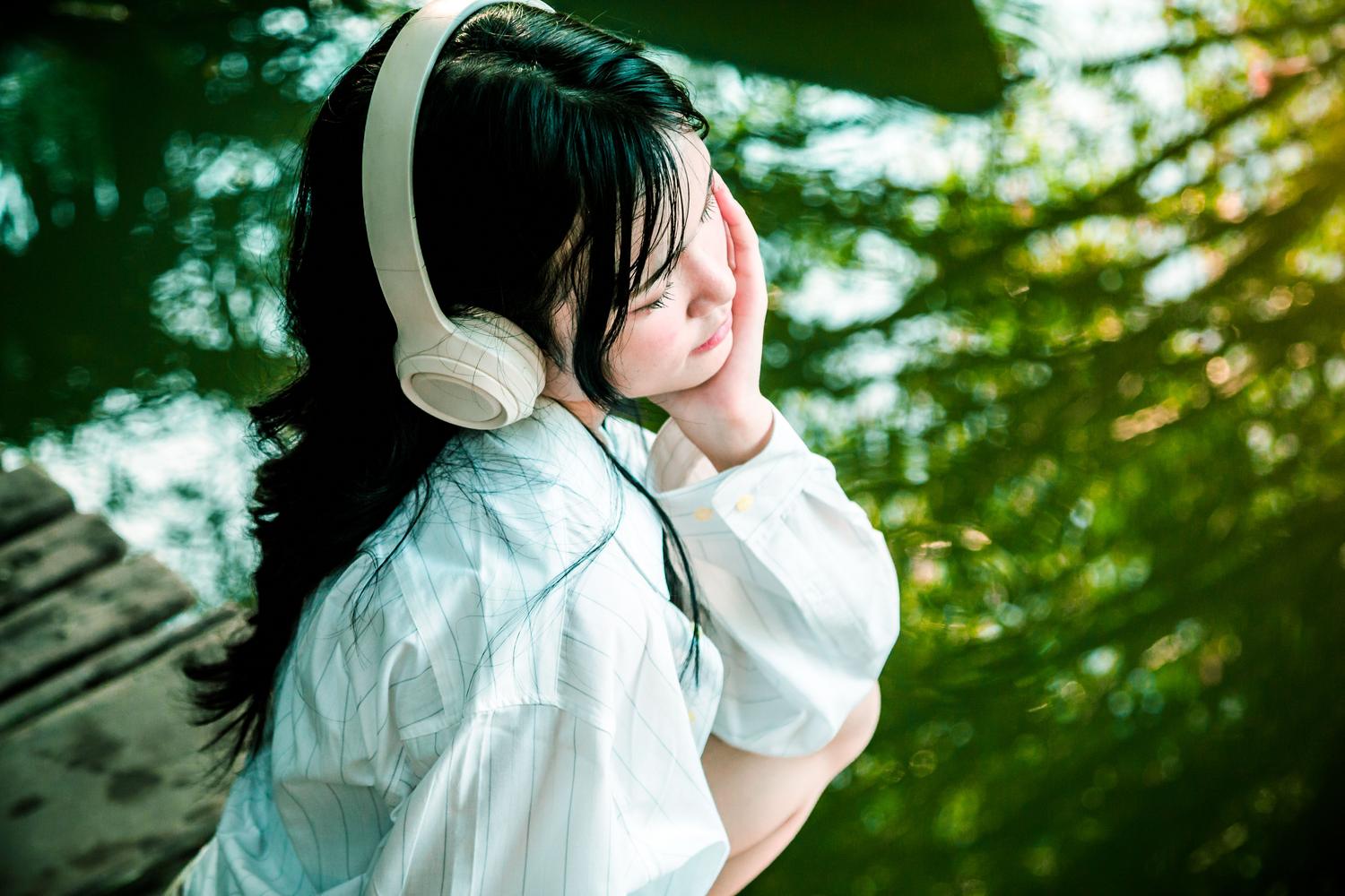Mujer disfrutando de la naturaleza y la música junto a un lago tranquilo.
