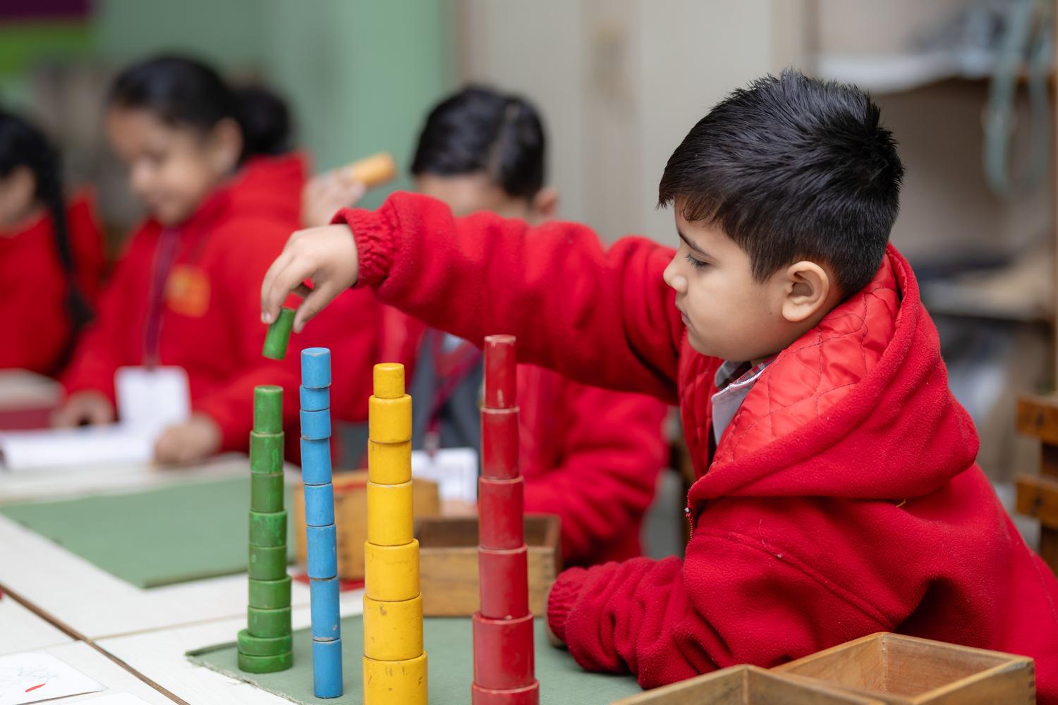 Niño pequeño aprendiendo matemáticas de forma lúdica mediante el uso de bloques de colores en un aula de educación infantil.