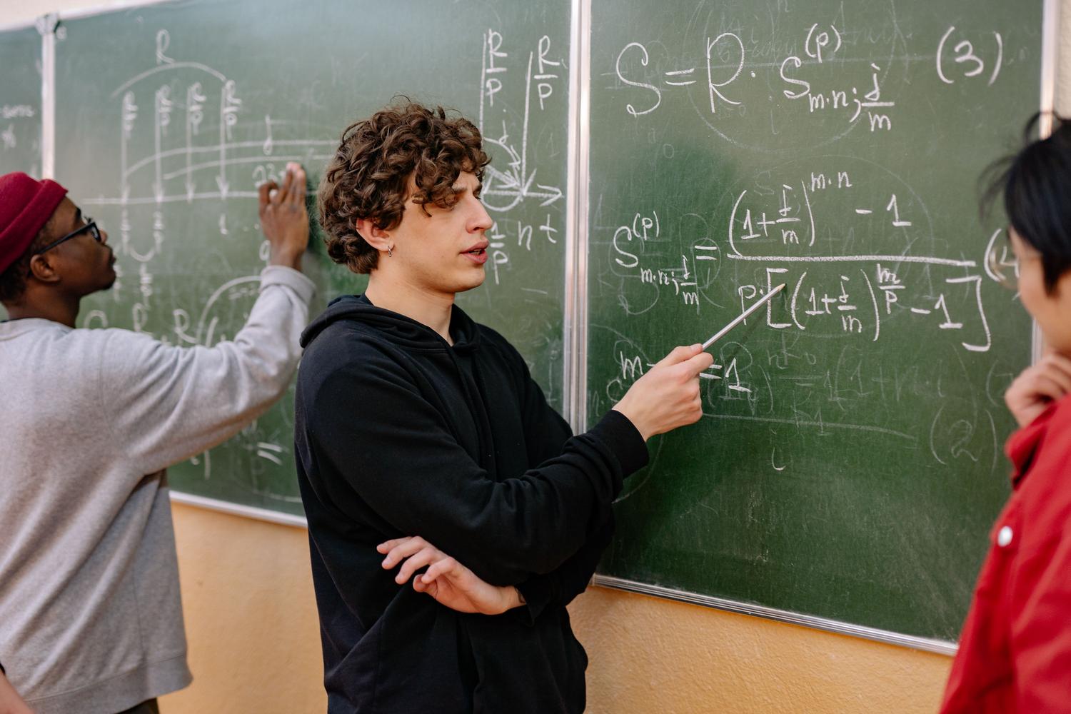 Estudiantes de nivel avanzado analizando ecuaciones matemáticas complejas y abstractas en un pizarrón universitario.