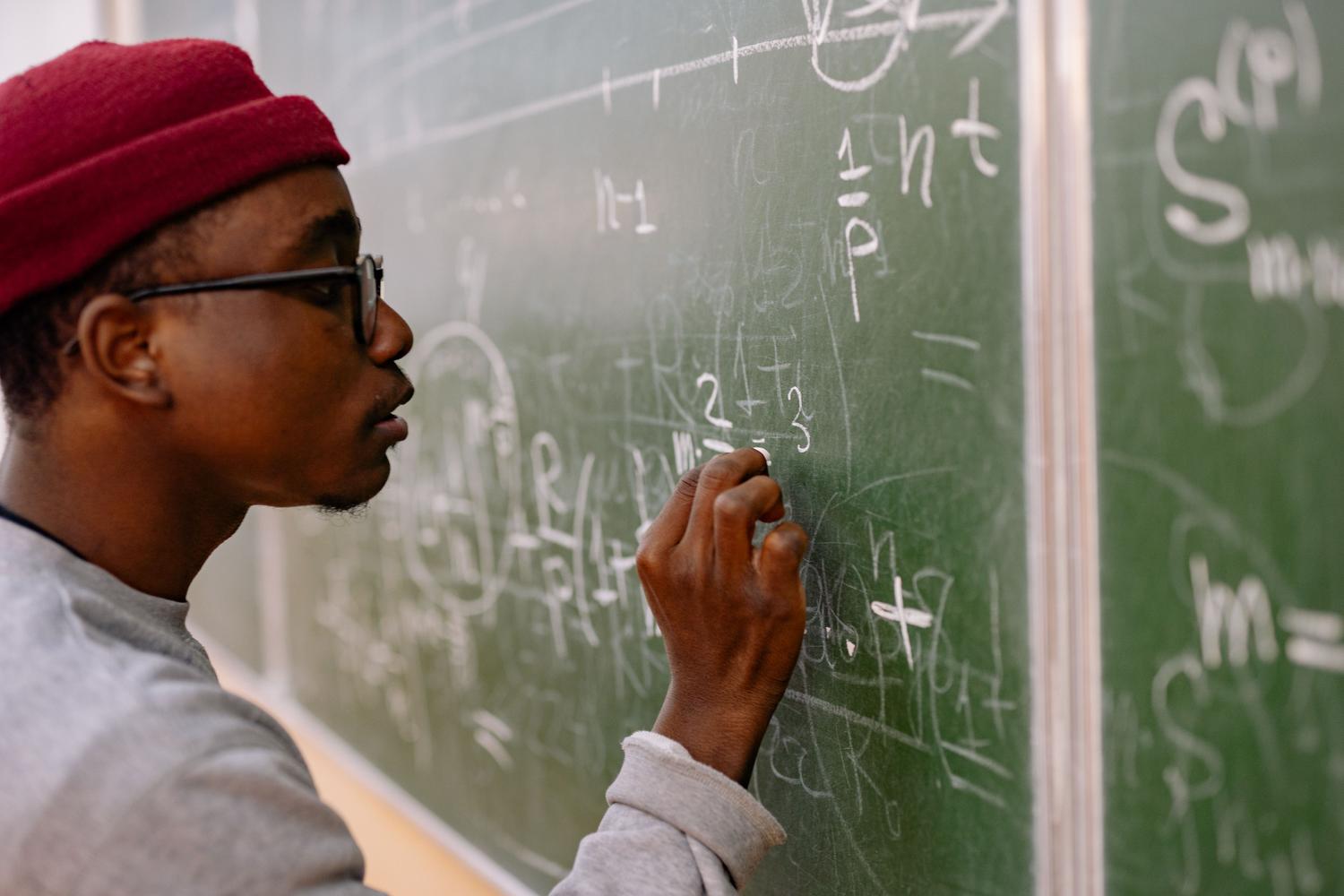 Joven estudiante de bachillerato concentrado resolviendo problemas matemáticos complejos en la pizarra.