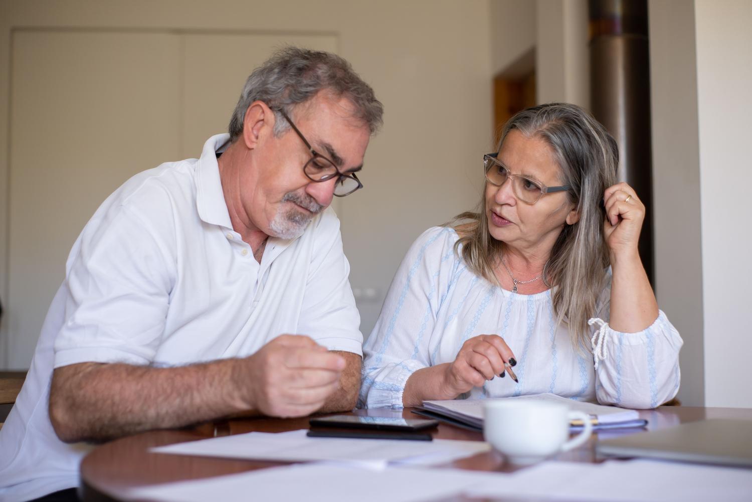 Pareja de personas mayores revisando documentos financieros y planificando su jubilación en casa